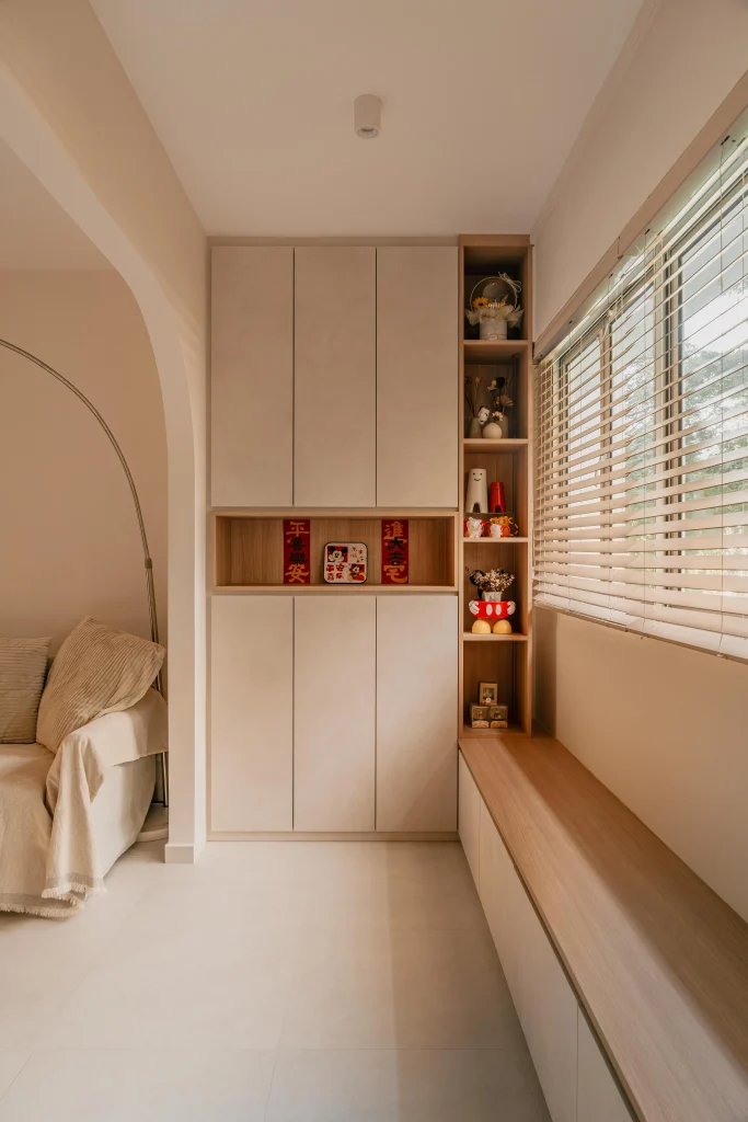Custom floor-to-ceiling beige built-in cabinets at 520 Jurong West St 52, featuring wooden display shelves, an open niche with red decor, and a long wooden window bench next to horizontal blinds.