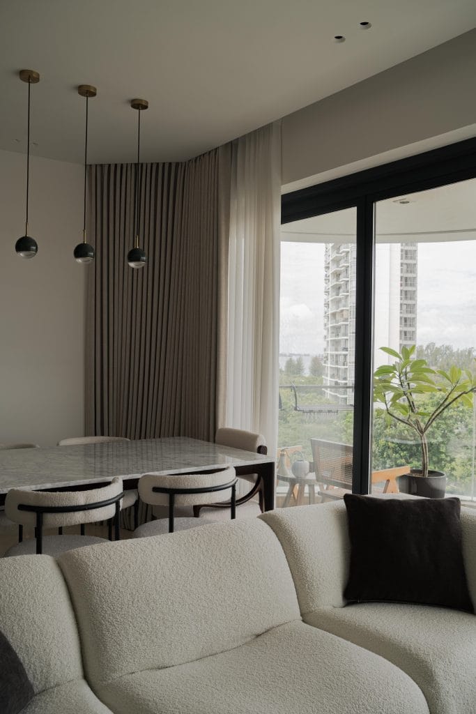 Modern organic living and dining room at The Amber Sanctuary featuring a curved bouclé sofa, a marble dining table, and a balcony with city views.