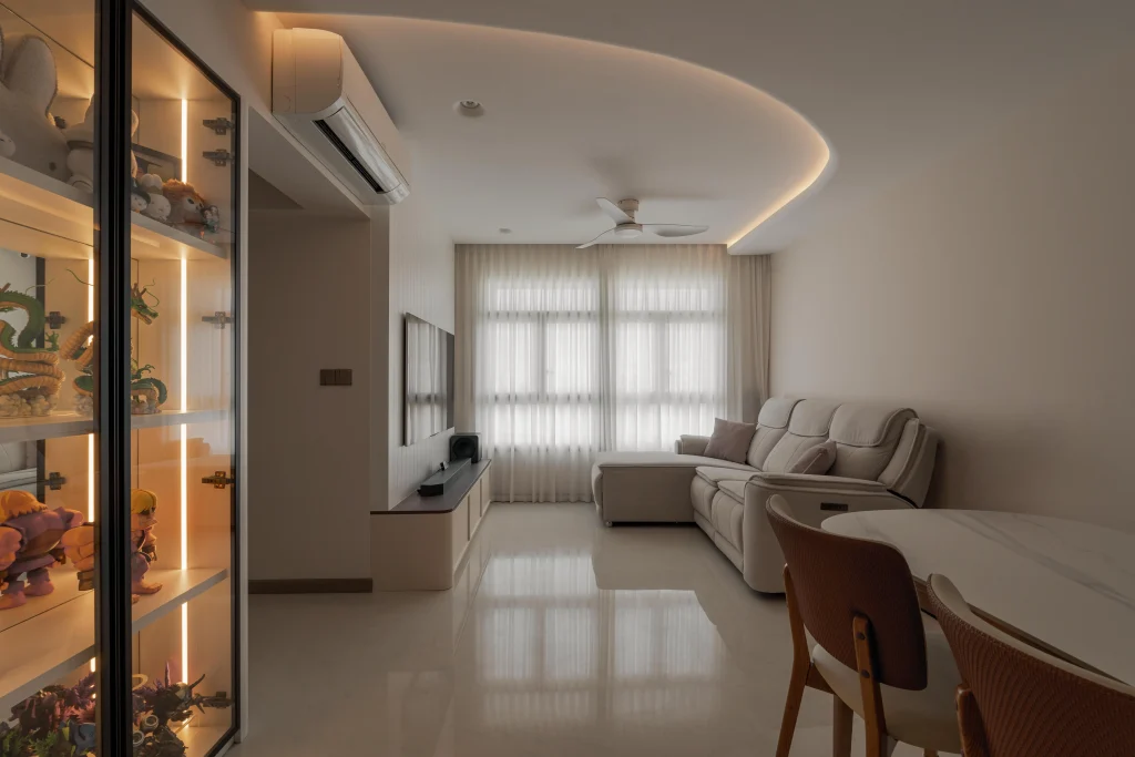 A wide view of a modern, bright living and dining space at 322A Tengah Drive, showcasing an illuminated glass display cabinet filled with figurines, a sleek TV console, and a comfortable cream sectional sofa.
